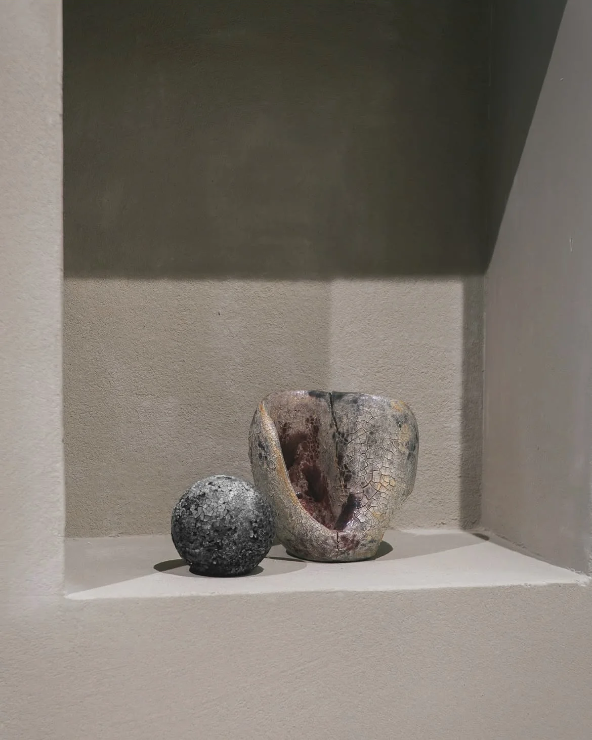 Two textured sculptural forms in a light-colored wall niche
