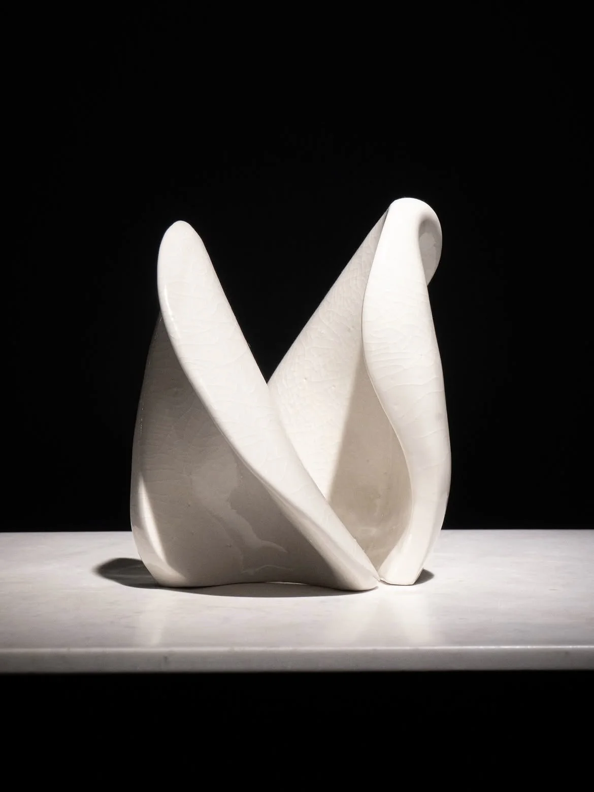 Curved white ceramic forms arranged on a lit platform