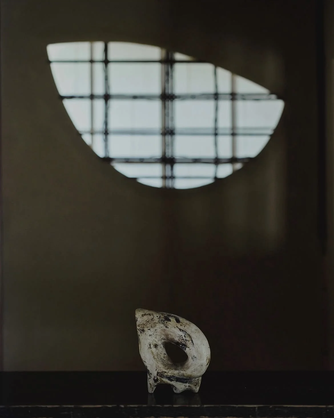 A small sculptural form beneath the light from a circular window