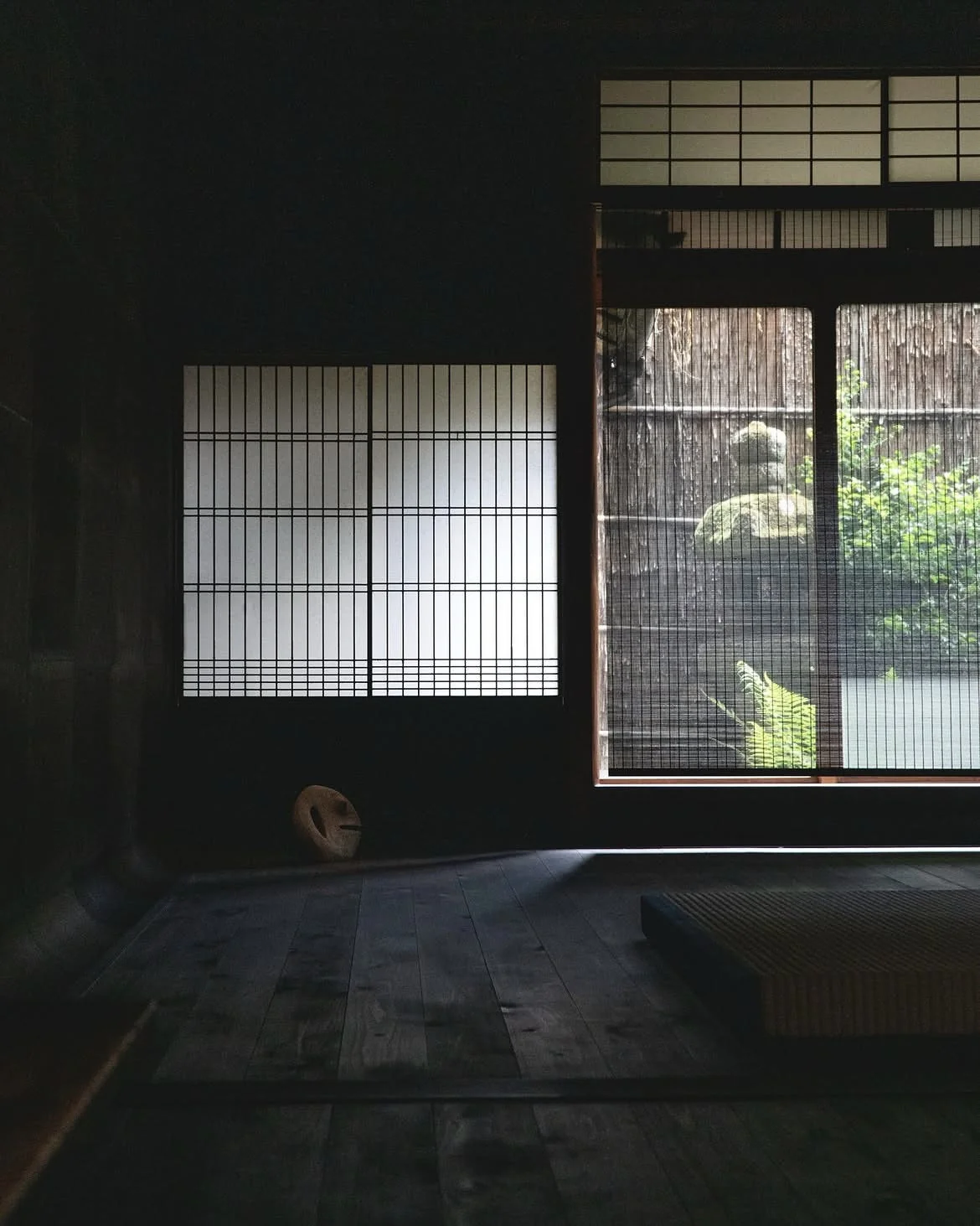 A quiet room with screens, a garden view and sculptural objects