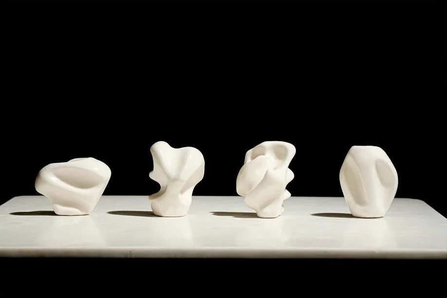 Four white hand-formed sculptures arranged across a platform